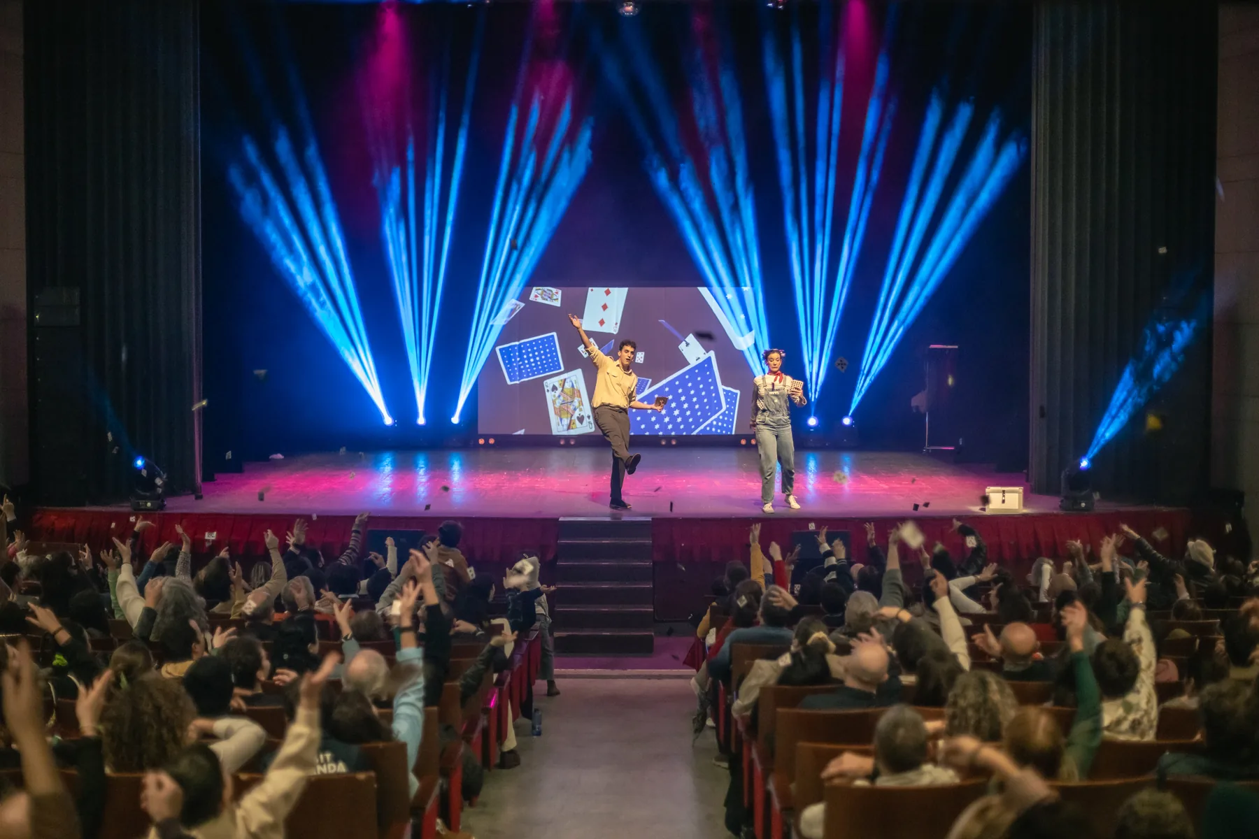 Fabio en el escenario de un teatro lleno, con el público levantando las manos mientras caen cartas
